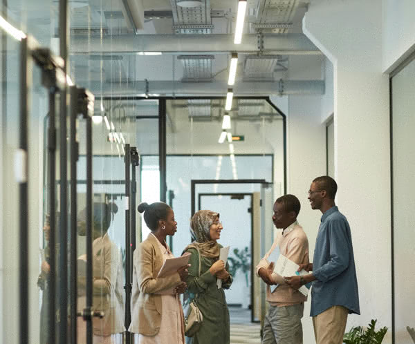 Four professionals engage in a friendly discussion in a modern office corridor.