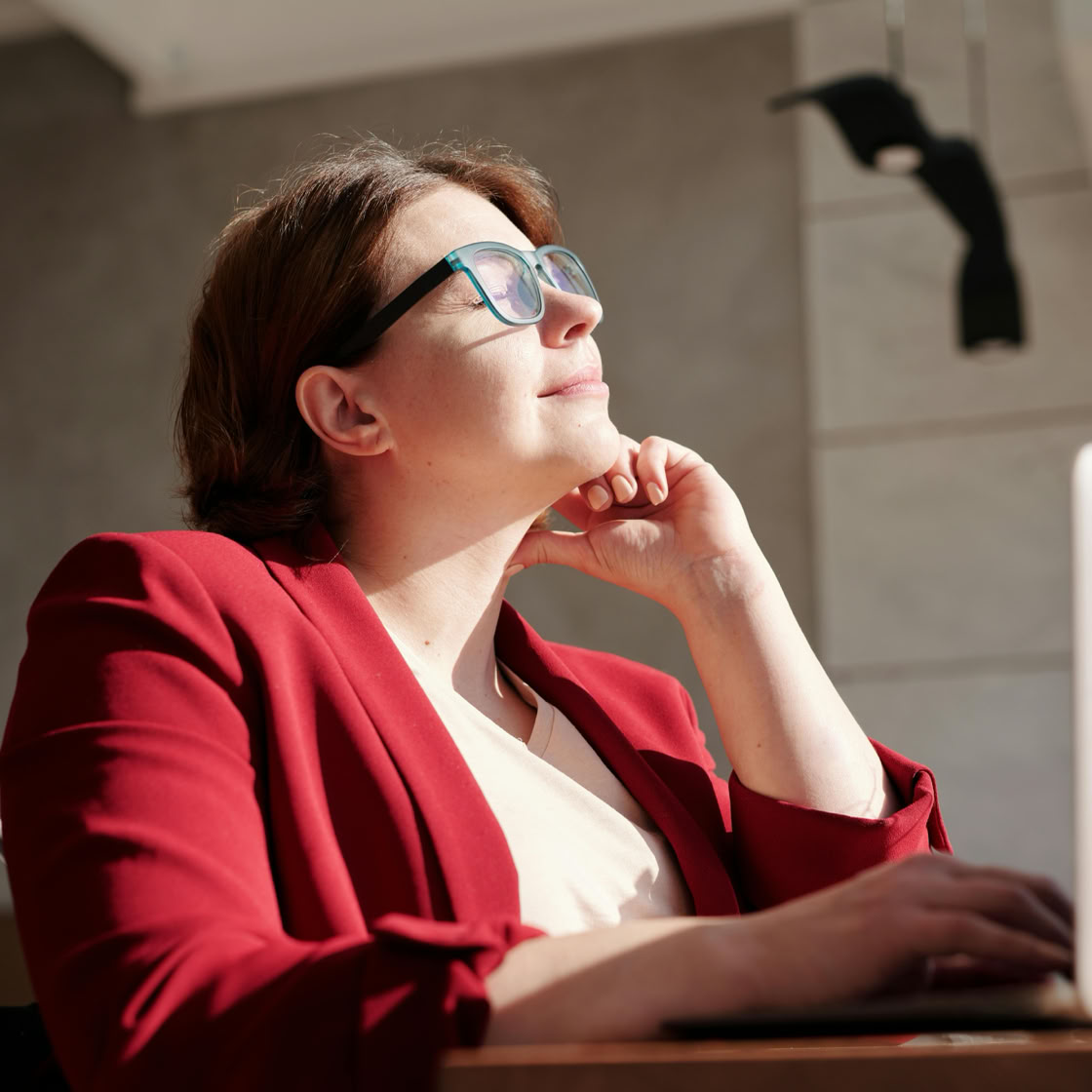 Woman in wheelchair wearing red suit and glasses, working on a laptop in a bright café.